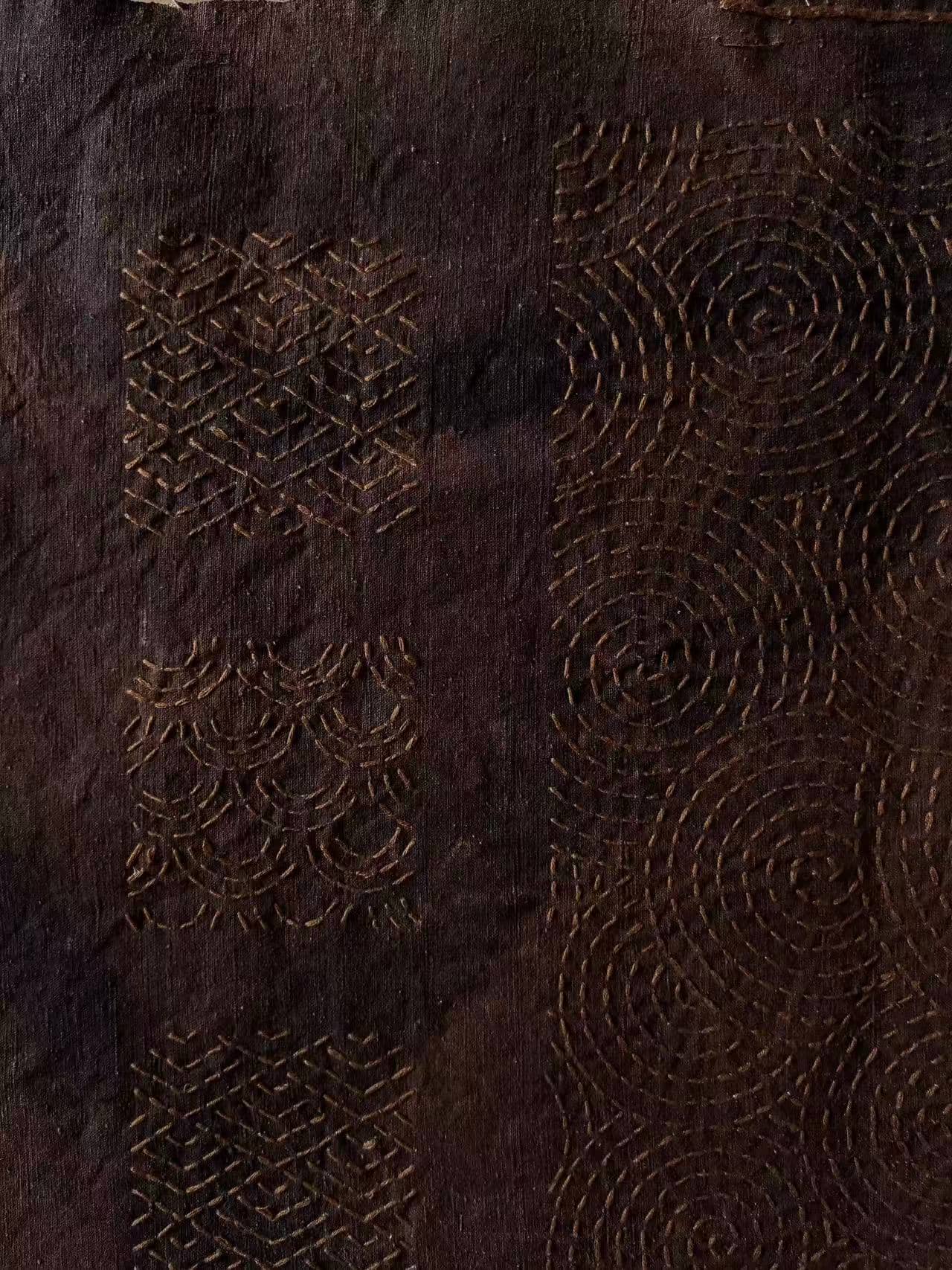 Geometric and circular stitched patterns on a dark textile by Echo Yu